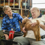 Senior Companion program volunteer Raymond Ruth, left, and Samuel Jones pet one of Jones’ dogs, Grizz, as they spend time together.
