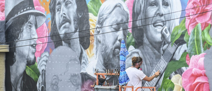 Artist Steven Teller paints the strings of Derek Trucks’ guitar as he works on the Johnny Sandlin mural this week.
